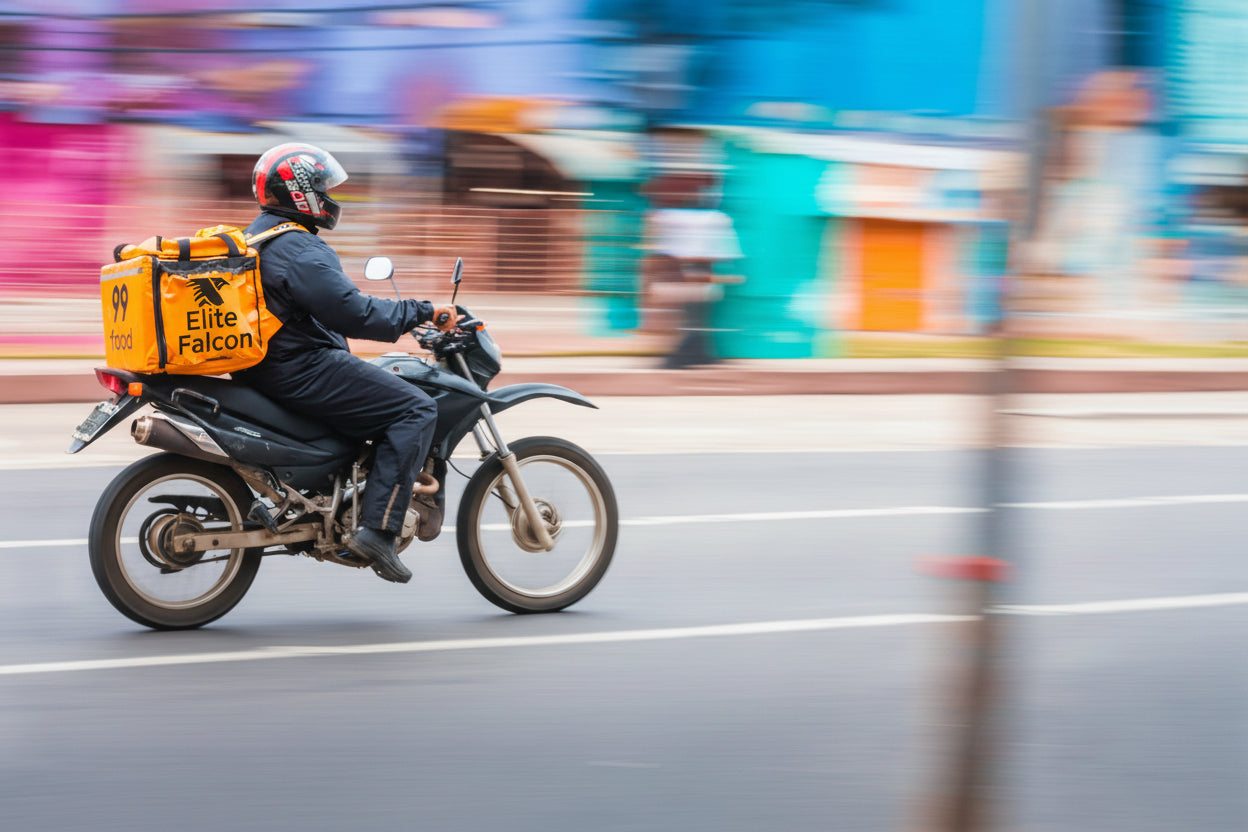 Person riding a motorcycle with a delivery bag on a city street
